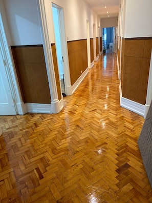 A hallway with wooden parquet flooring, white walls, and brown wainscoting.