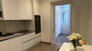 Una cocina moderna con armarios blancos, horno empotrado y comedor con mesa y jarra de flores.