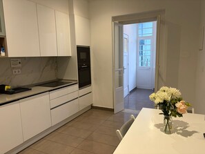 Ett modernt kök med vita skåp, en inbyggd ugn och en matplats med ett bord och en vas med blommor.