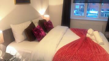 A hotel room with a bed, a nightstand, a lamp, a painting on the wall, and a window with blinds.