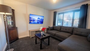Una sala de estar con un sofá, una mesa baja con flores, un televisor y una lámpara.