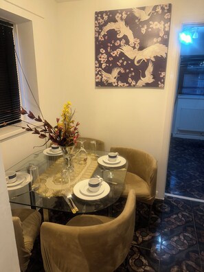 Uma sala de jantar com mesa de vidro, cadeiras e um vaso de flores.