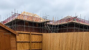 Un cortile con erba sintetica, una recinzione in legno e un edificio in costruzione.