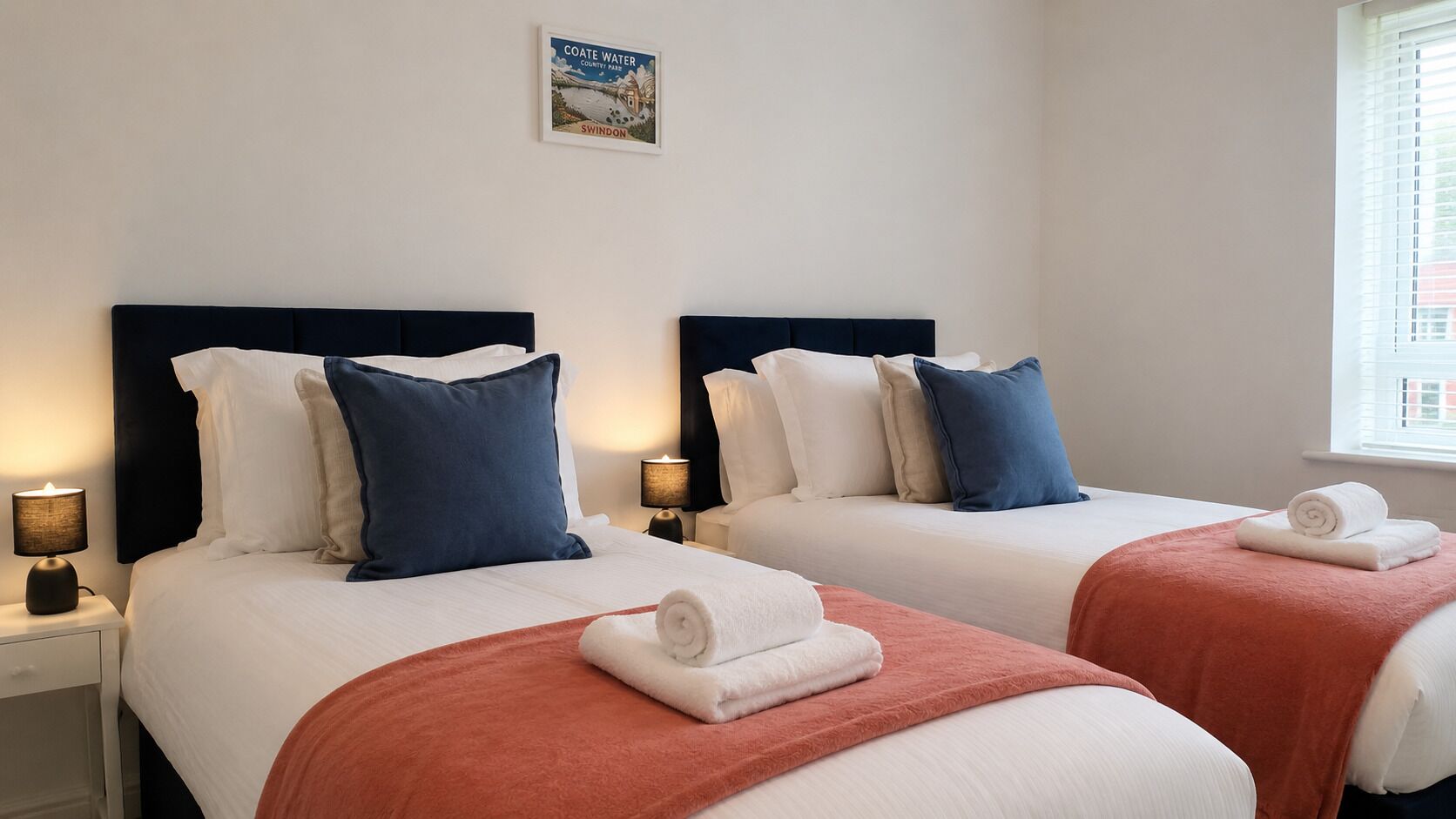 A hotel room with two beds, each with a headboard, bedside tables with lamps, and a framed picture on the wall.