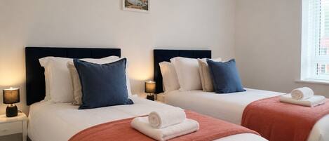 A hotel room with two beds, each with a headboard, bedside tables with lamps, and a framed picture on the wall.