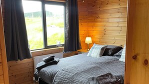 Un dormitorio de cabaña de madera con cama, mesita de noche, lámpara y ventana con cortinas.