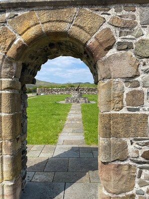 An arched stone structure with a pathway leading to a stone wall and grassy area.