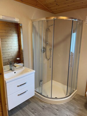 Ein modernes Badezimmer mit einer einteiligen Glasdusche, einem weißen Waschtisch und einer Holzzahlendecke.