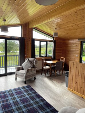 Eine Holzhütte mit Essbereich, einem karierten Teppich und Blick ins Freie.