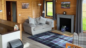 Interior de una cabaña de madera con sofá, chimenea, mesa de comedor y un cubo de basura.
