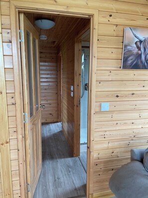Un intérieur en bois avec un couloir menant à une salle de bain, un canapé gris et un ventilateur de plafond.