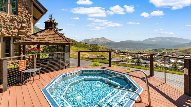 A hot tub on a wooden deck with a view of mountains and a town in the background. - Columbine 2308 (Crested Butte)