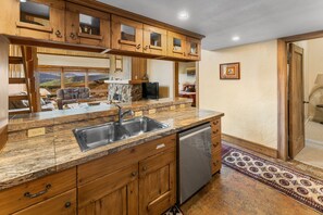 A kitchen with wooden cabinets, a granite countertop, a stainless steel sink, and a dishwasher. - Columbine 2308 (Crested Butte)