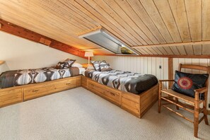 A cozy attic bedroom with a sloped ceiling, a wooden bed with patterned bedding, a chair with a cushion, and a small table with a lamp. - Columbine 2308 (Crested Butte)