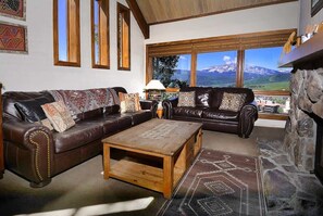 A living room with two leather sofas, a wooden coffee table, and a view of mountains through large windows. - Columbine 2308 (Crested Butte)