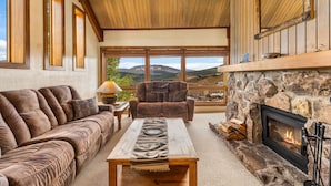 A cozy living room with a stone fireplace, a sofa, a coffee table, and a view of the mountains. - Columbine 2308 (Crested Butte)