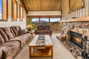 A cozy living room with a stone fireplace, a sofa, a coffee table, and a view of the mountains. - Columbine 2308 (Crested Butte)