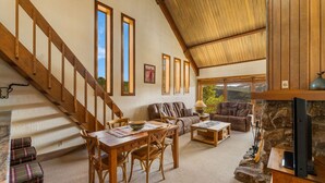 A spacious living room with a wooden staircase, a stone fireplace, and a large window offering a view of the outdoors. - Columbine 2308 (Crested Butte)