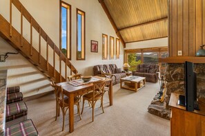 A spacious living room with a wooden staircase, a stone fireplace, and a large window offering a view of the outdoors. - Columbine 2308 (Crested Butte)
