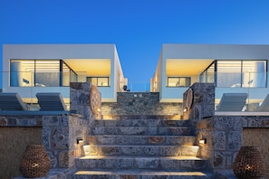 A modern building with a stone staircase leading to a balcony with lounge chairs. - MT7 Panoramic Sea View Villa, Villa (Limenas Chersonisou)