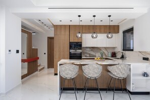 A modern kitchen with a marble countertop, wooden cabinets, and pendant lighting. - MT7 Panoramic Sea View Villa, Villa (Limenas Chersonisou)