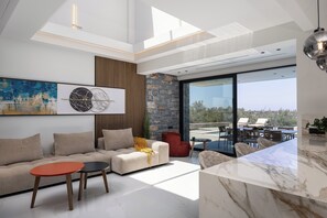A modern living room with a sofa, two tables, a red chair, a stone wall, and a large window. - MT7 Panoramic Sea View Villa, Villa (Limenas Chersonisou)