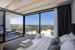 A modern bedroom with a large bed, a balcony with a view, and a dining area. - MT7 Panoramic Sea View Villa, Villa (Limenas Chersonisou)