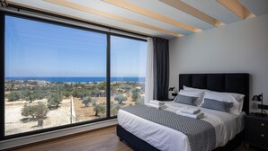 Ein Schlafzimmer mit großem Fenster, einem Bett mit weißer und grauer Bettwäsche, einem dunklen Kopfteil und einem Nachttisch mit Lampe.