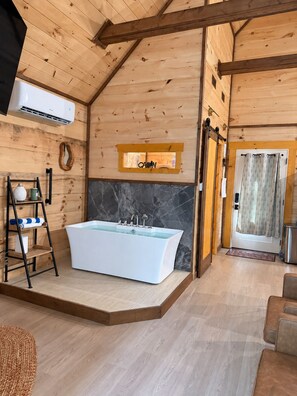 A wooden cabin interior with a large bathtub, a wooden ladder, a door with a curtain, and a small shelf with items. - Romantic Cabin • Fireside Jacuzzi + Hot Tub (Sevierville)