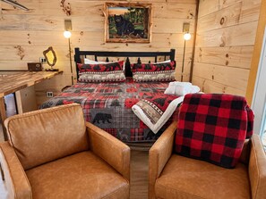 Ein gemütliches Blockhauszimmer mit einem Bett, zwei Ledersesseln, einem Holztisch und einem Bild an der Wand.