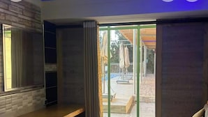 Una stanza con un tavolo di legno, una panca e una porta scorrevole in vetro che dà su un'area esterna con piscina e ombrelloni.