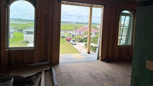 Quarto com paredes de madeira e uma grande porta aberta que dá para área externa com vista para casas e uma estrada.