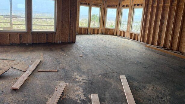 Quarto com janelas amplas, vigas de madeira aparentes e piso de concreto.