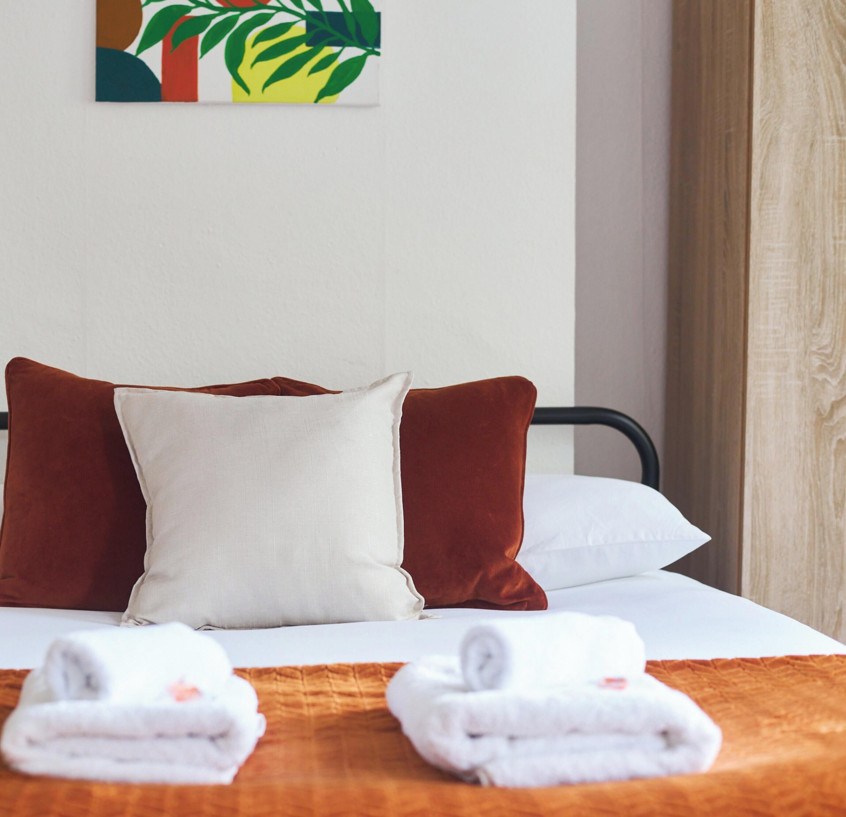 Een hotelkamer met een bed, twee kussens, een deken en twee handdoeken.