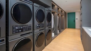Een wasserette met meerdere wasmachines en drogers, een groene deur en een houten vloer.