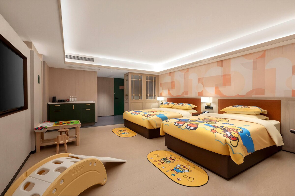 A hotel room with two beds, a desk, a chair, and a play area.