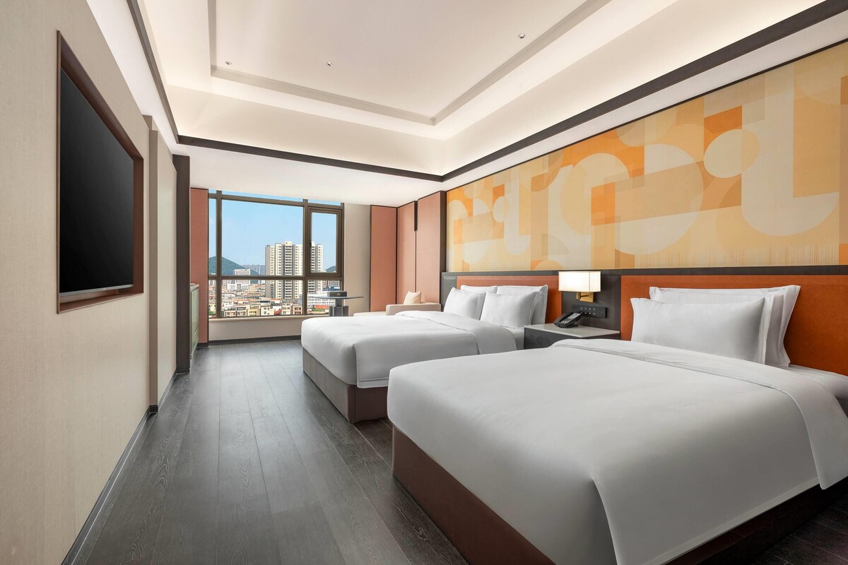 A hotel room with two beds, a large window, and a city view.