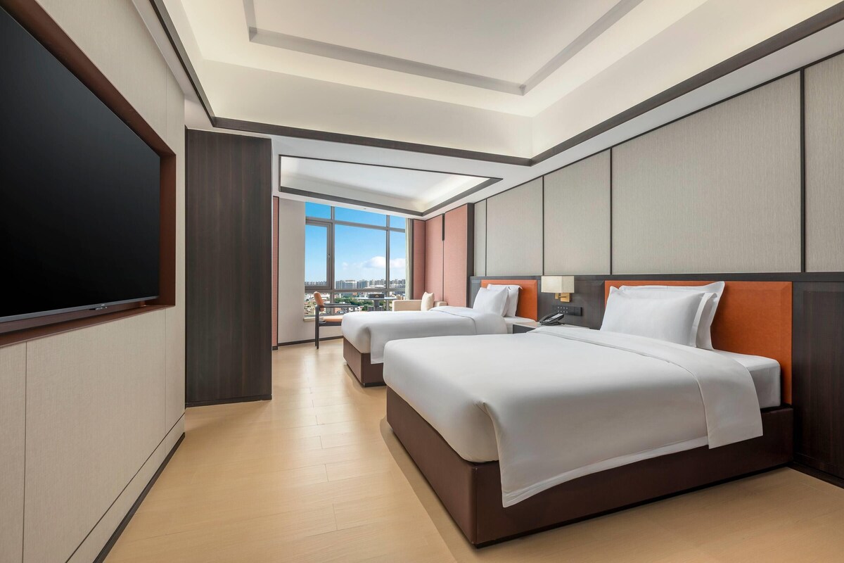 A hotel room with two beds, a TV, and a city view.