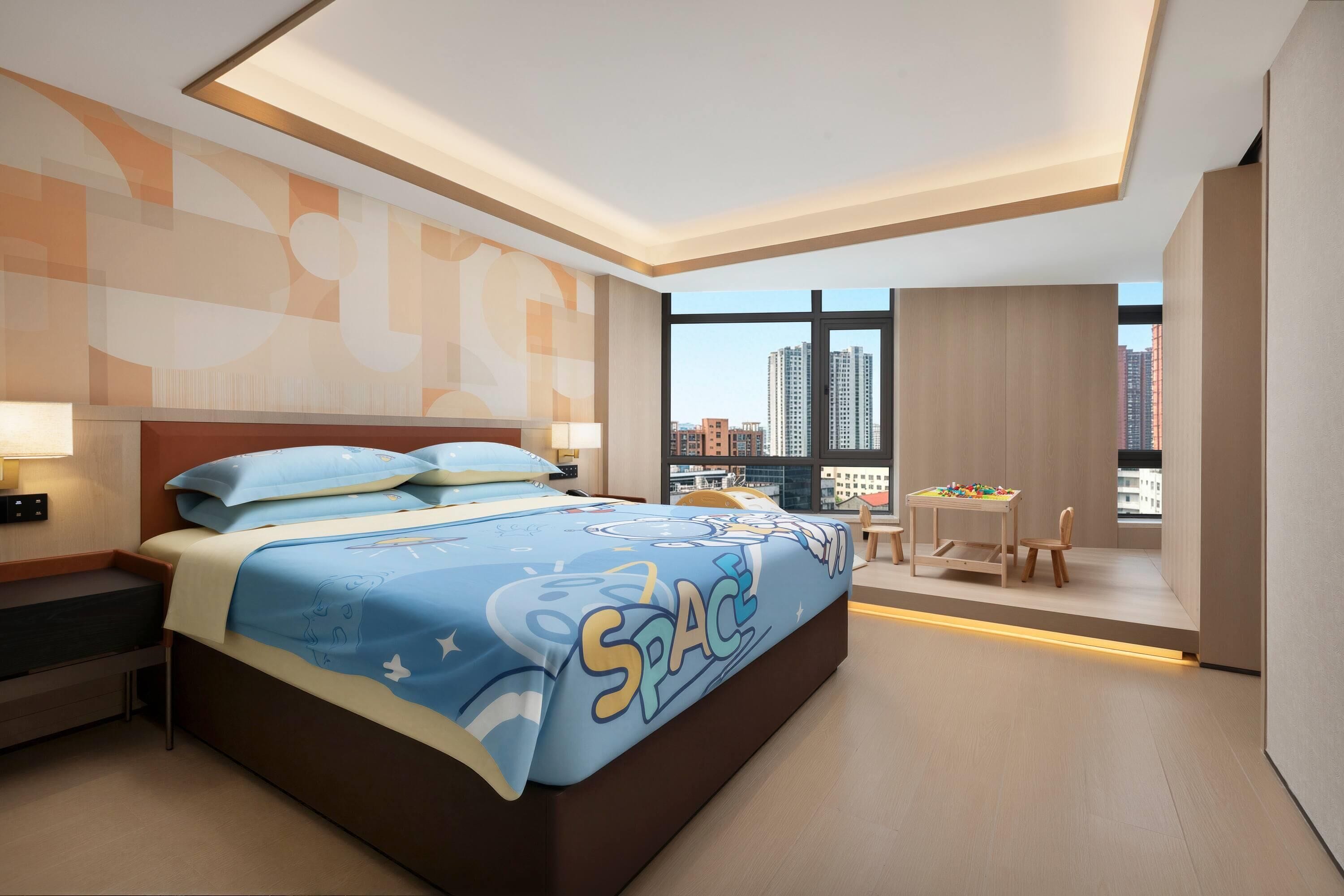 A modern hotel room with a large bed, a desk, and a view of the cityscape.