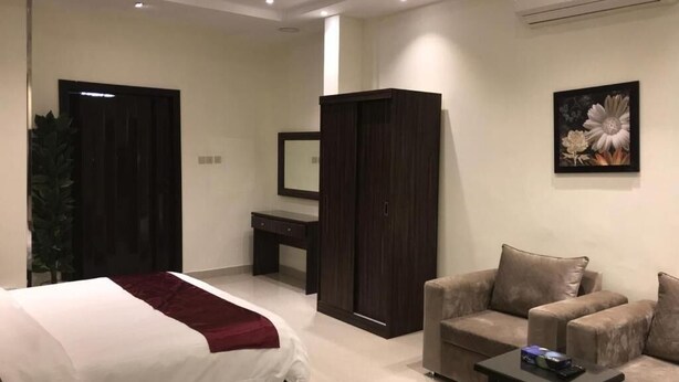 A hotel room with a bed, a desk, a wardrobe, a sofa, and a painting on the wall. - Rest Time Golden Hotel (Riyadh)