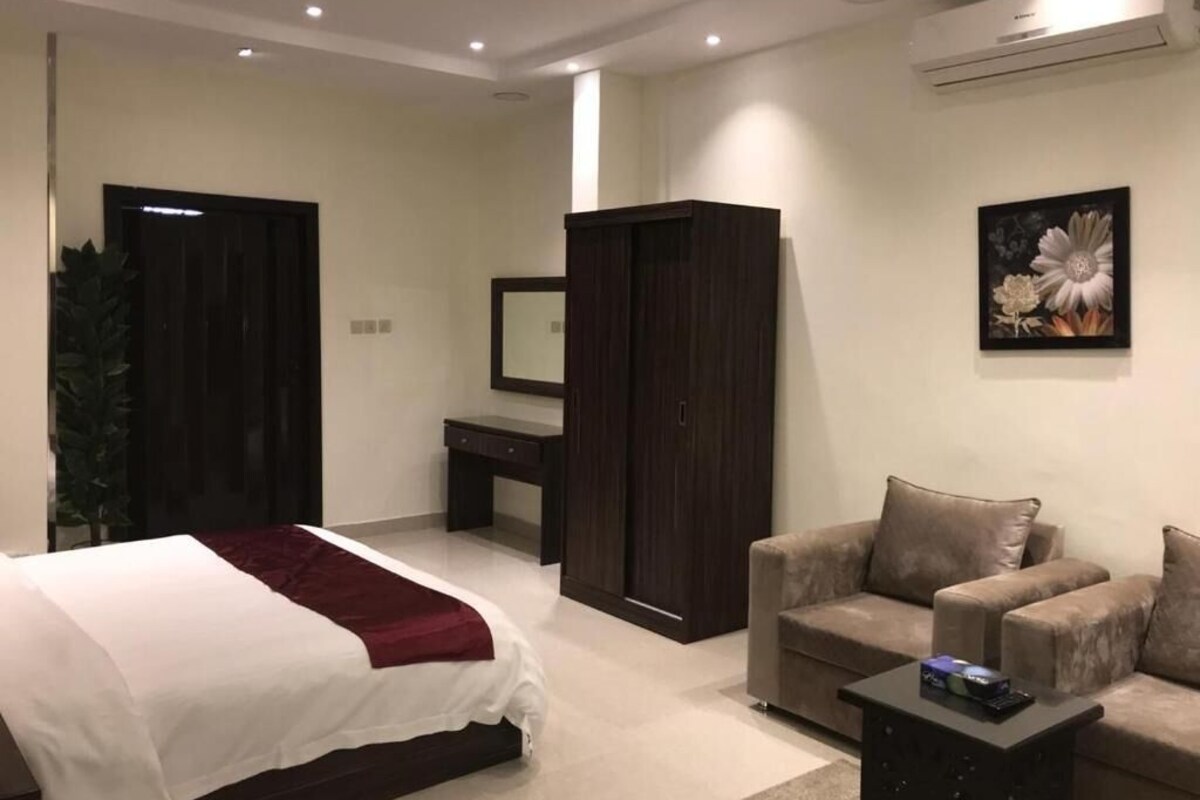 Ein Hotelzimmer mit Bett, Schreibtisch, Kleiderschrank, Sofa und einem Bild an der Wand.