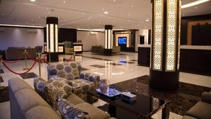 A lobby with sofas, a reception desk, a TV screen, and a decorative pillar. - Rest Time Golden Hotel (Riyadh)