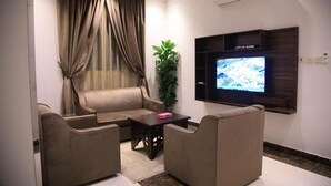 A living room with a sofa, two armchairs, a coffee table, a TV mounted on the wall, a plant, and a window with curtains. - Rest Time Golden Hotel (Riyadh)