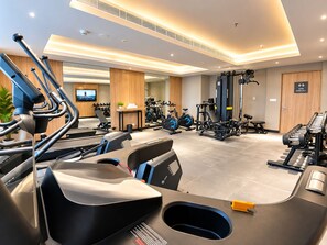 Un gimnasio moderno con diversos equipos de ejercicio, un televisor y un letrero que indica que está abierto las 24 horas.
