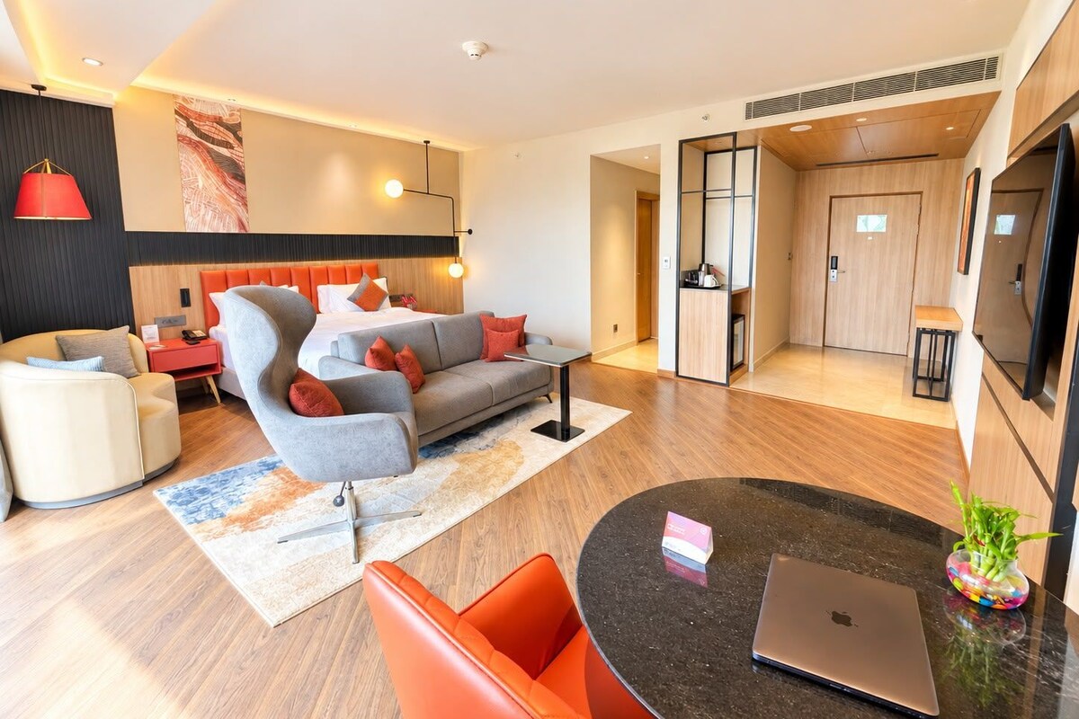 Et moderne hotelværelse med sofa, lænestol og spiseplads med en bærbar computer og en vase.
