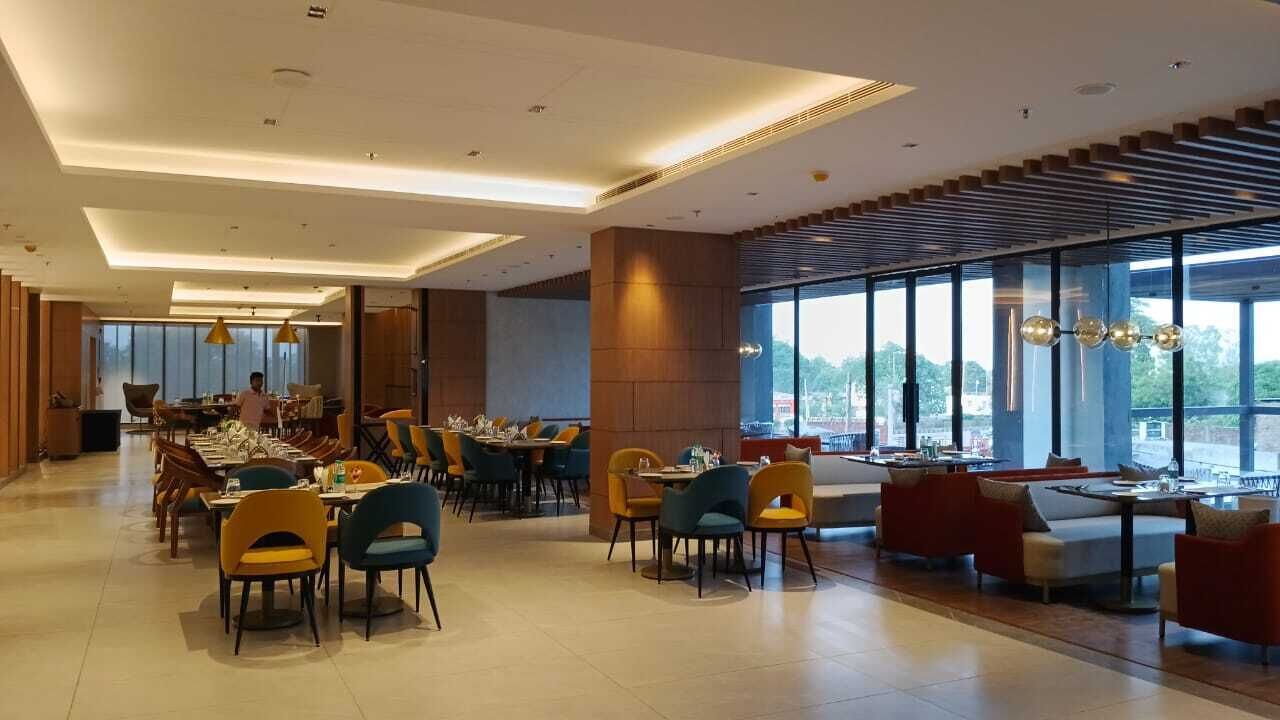 Un espace repas moderne doté de plusieurs tables et chaises, de grandes fenêtres et offrant une vue sur l’extérieur.