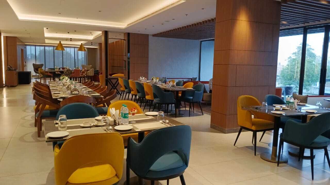 A modern dining area with multiple tables and chairs, large windows, and a high ceiling.