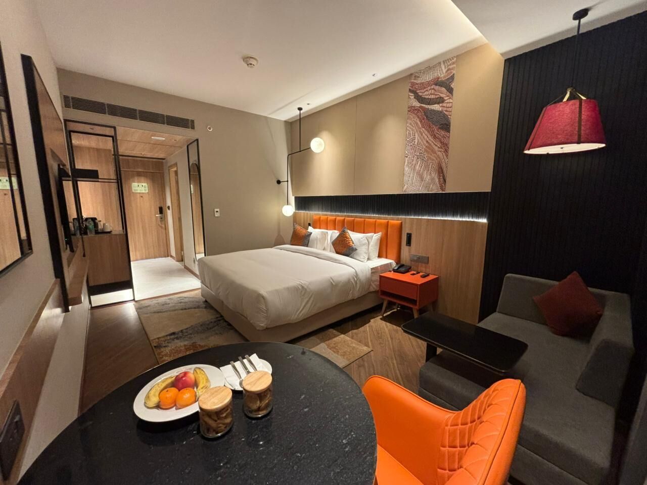 Habitación de hotel con cama, escritorio, silla, mesa de comedor con fruta y sofá.