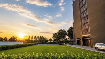 A modern building with a flat roof, a well-maintained lawn, and a clear sky with the sun setting.