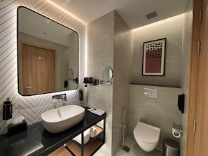 A modern bathroom with a large mirror, a white sink, a toilet, and a shower. - Ramada Encore By Wyndham Ayodhya Takpura (Faizabad)